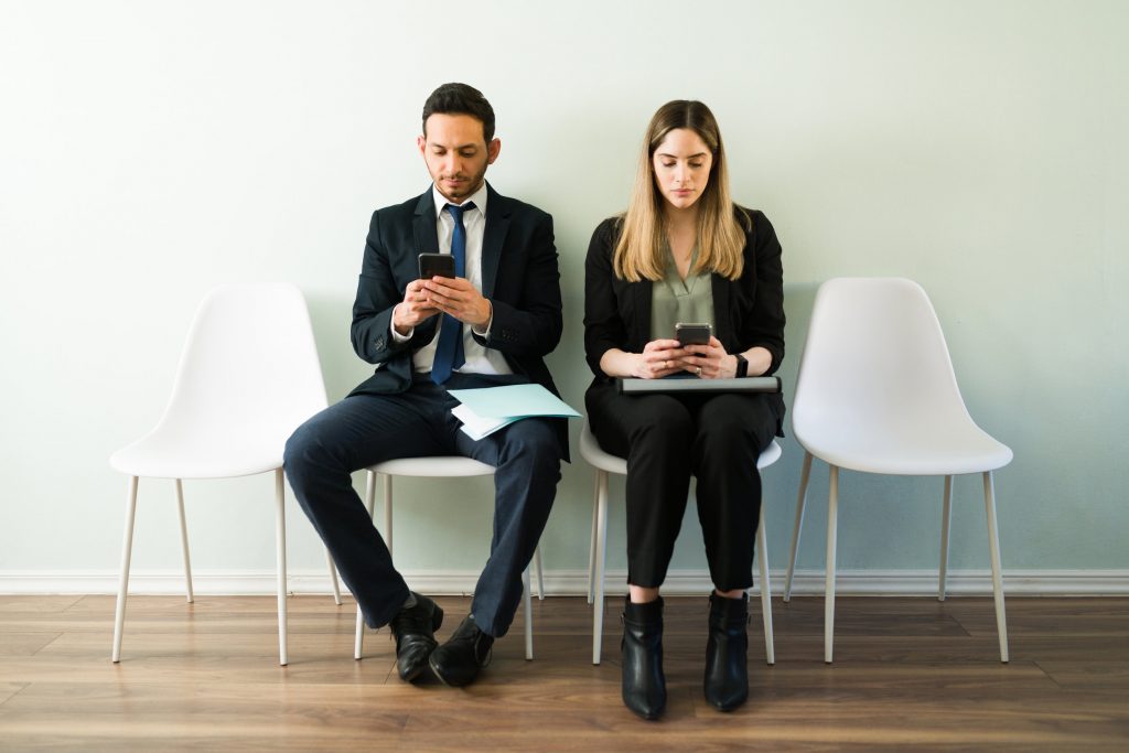Deux jeunes personnes sur leurs portables en attendant de participer à un entretien d'embauche en anglais
